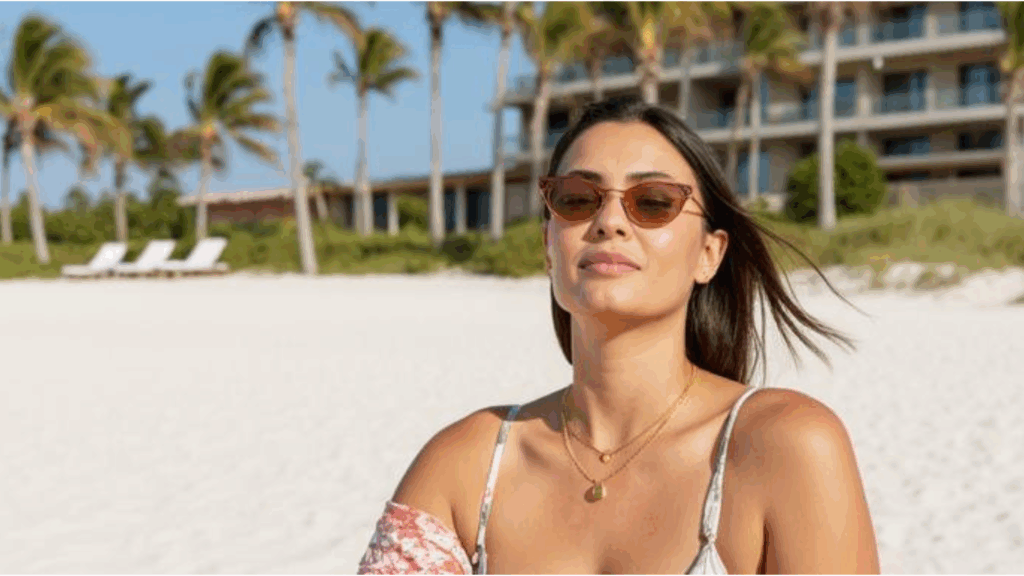 A woman wearing gold necklaces standing on a sunny beach, representing the financial freedom and independence of gold ownership.