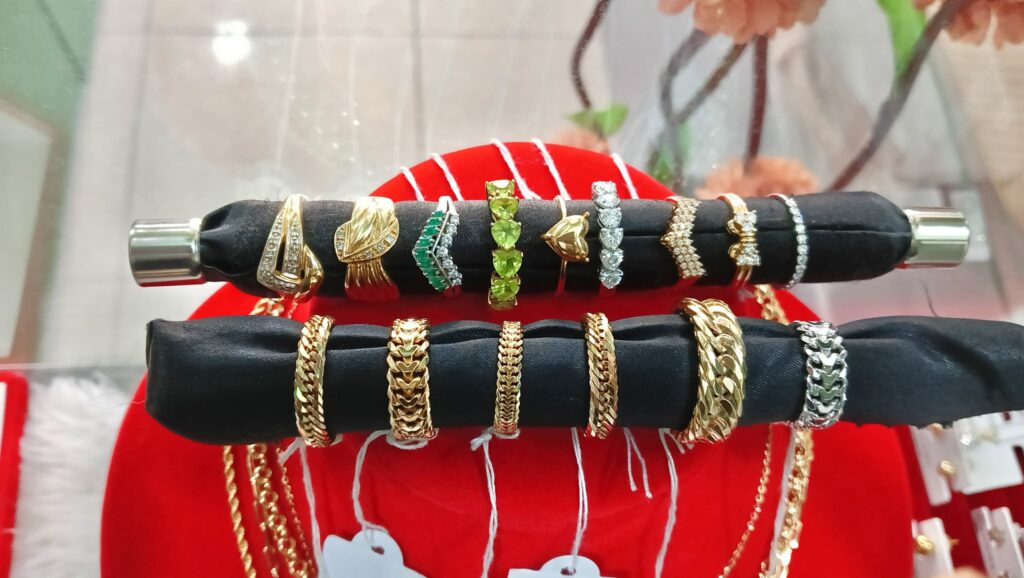 A premium display of various 18k and 24k solid Japan gold rings, including heart shapes, gemstone accents, and thick structural bands.